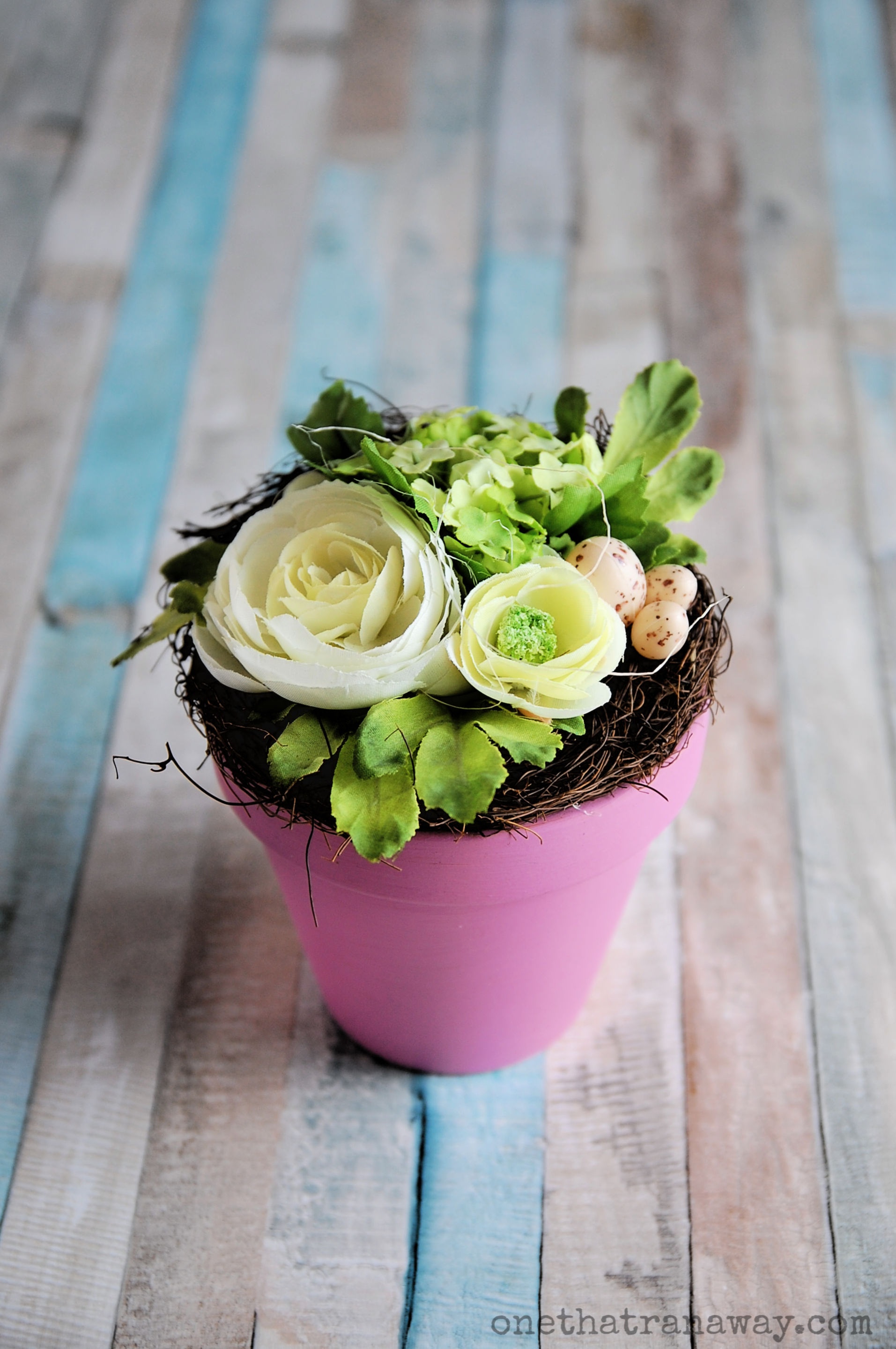 green and cream coloured flower bouquet in a pink flower pot on wooden surface