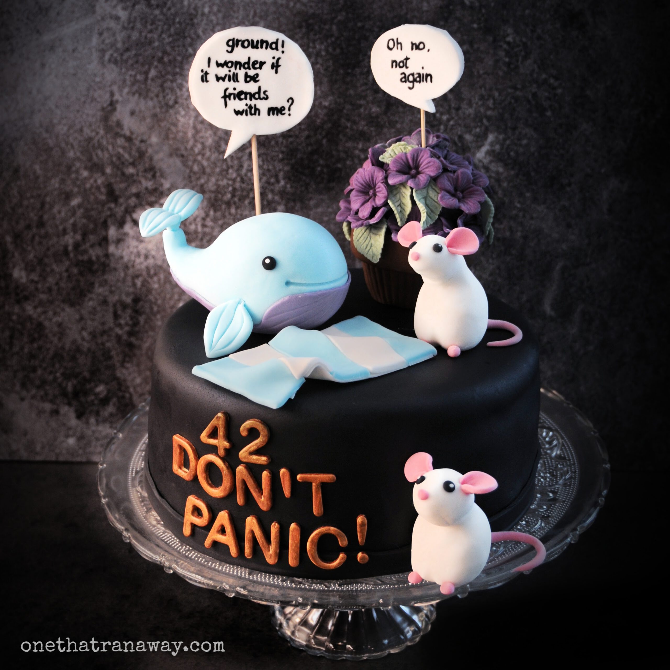 hitchhiker's guide to the galaxy themed cake covered with black fondant, a whale, a towel, two mice and a pot of petunias on top
