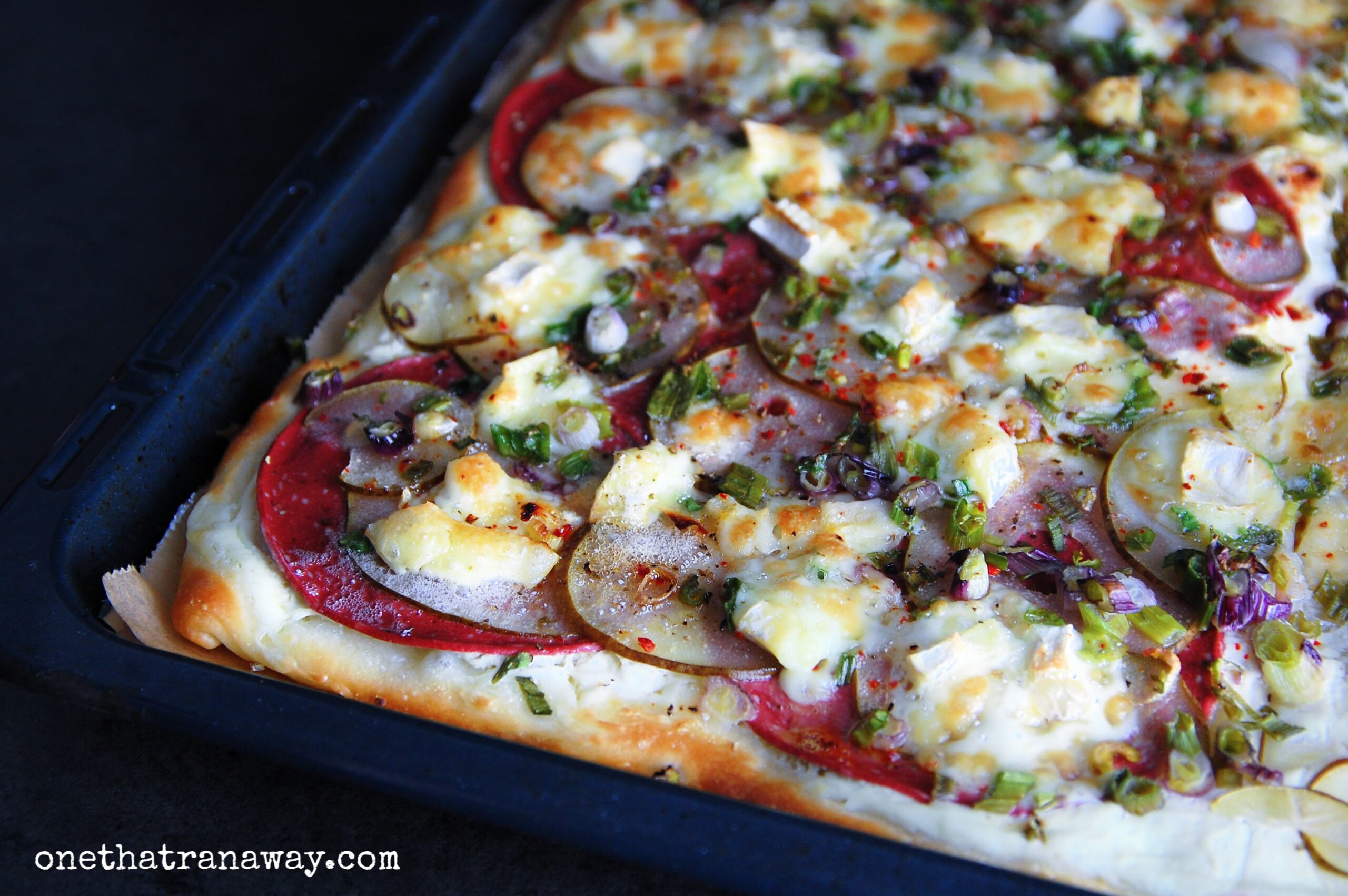 autumn pizza with brie, salami and pear on a black baking tray