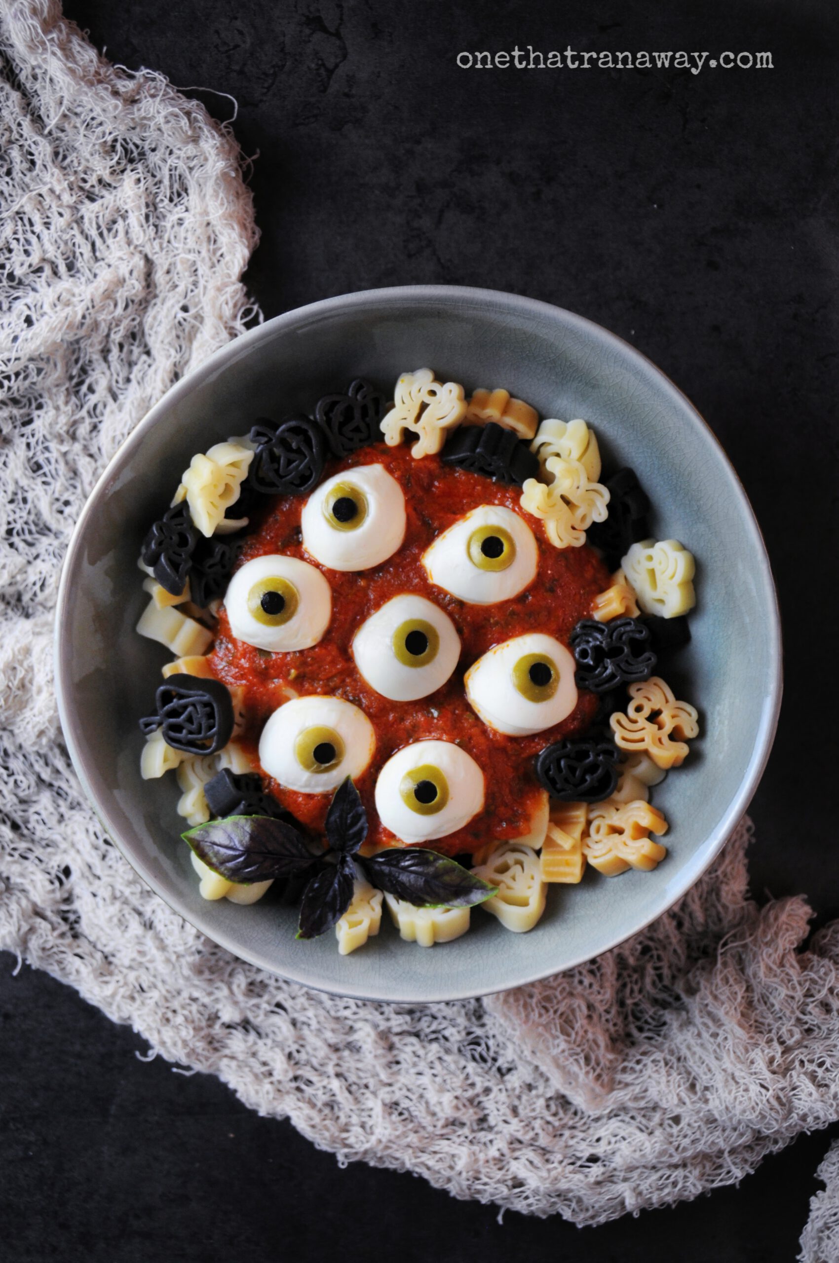a plate with Halloween shaped pasta and eyeballs made from mozzarella on a dark background
