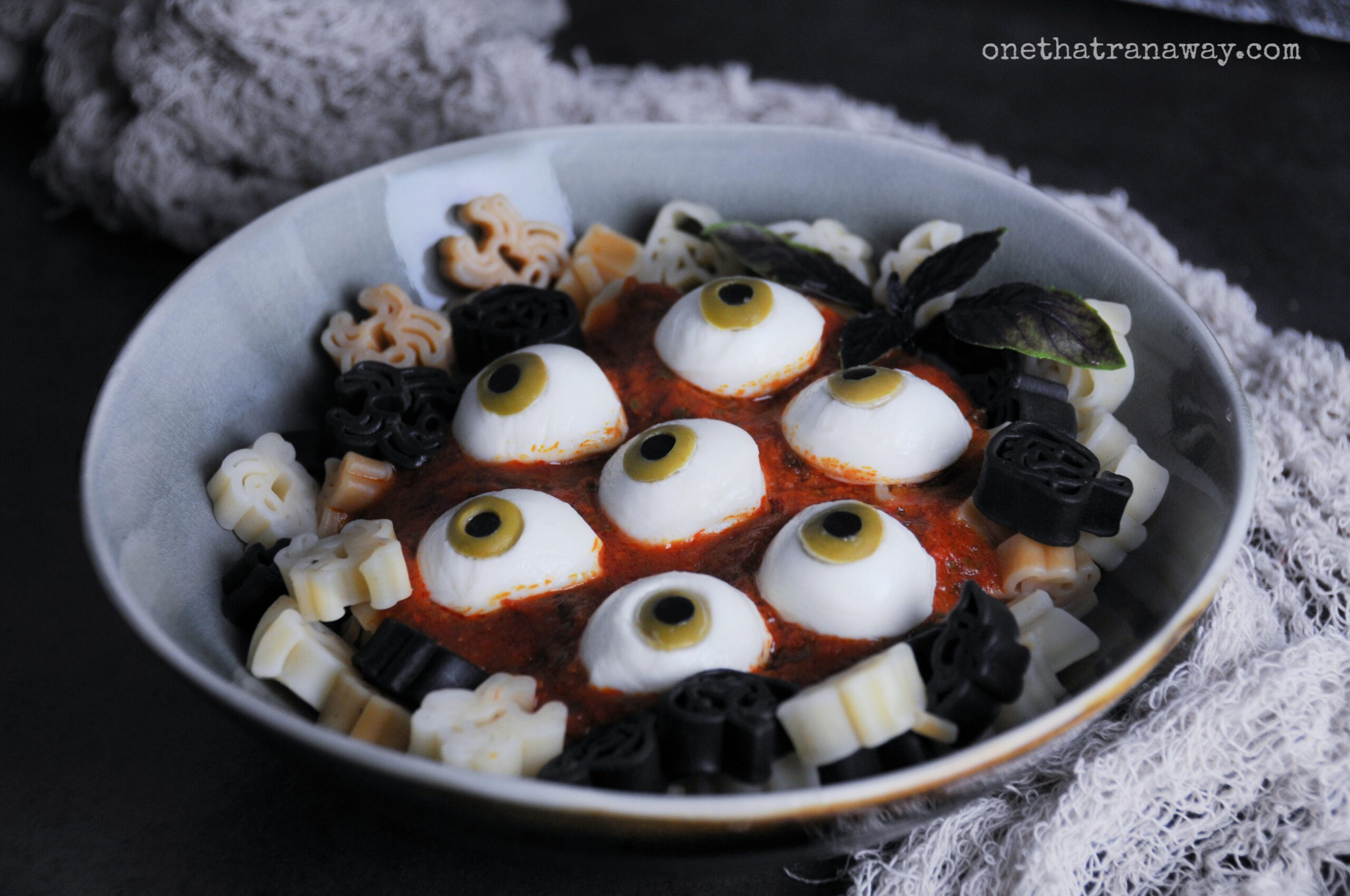 a plate with Halloween shaped pasta and eyeballs made from mozzarella on a dark background