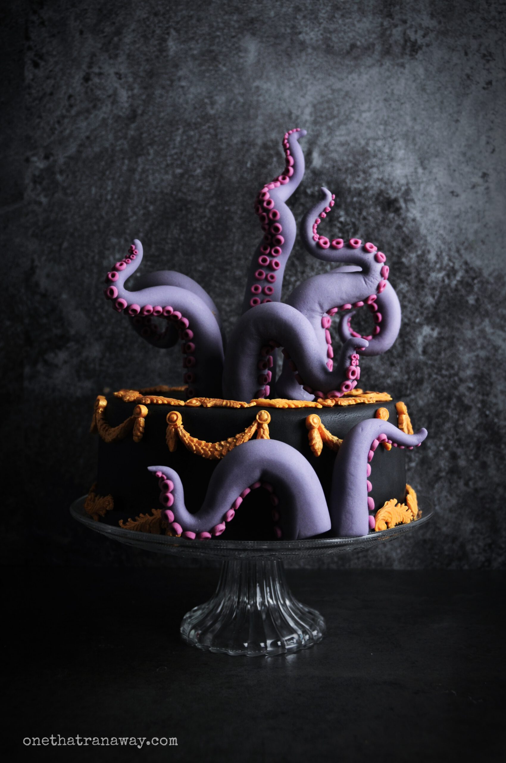 a black cake with purple fondant tentacles and gold ornaments on black background