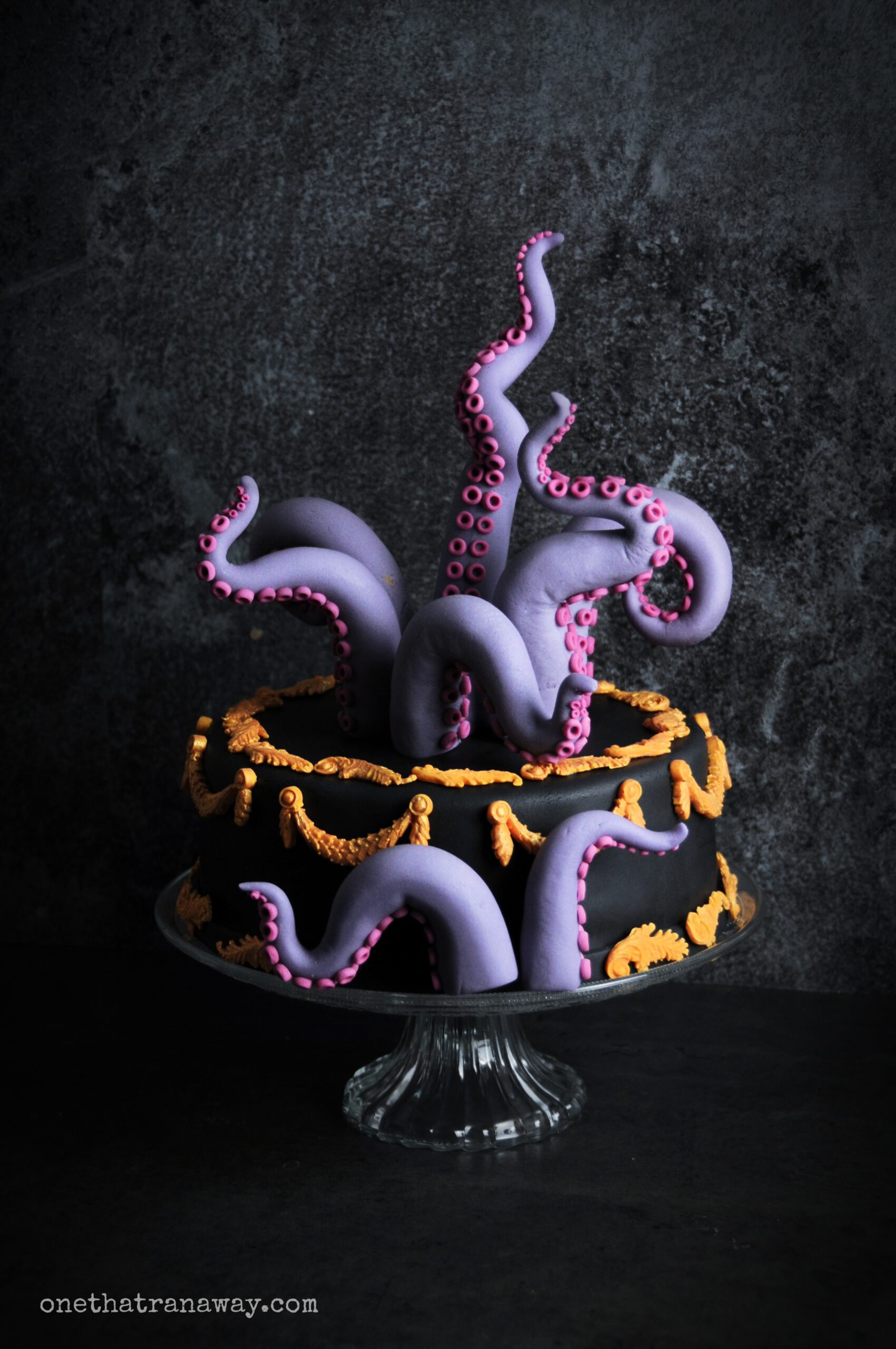 a black cake with purple fondant tentacles and gold ornaments on black background