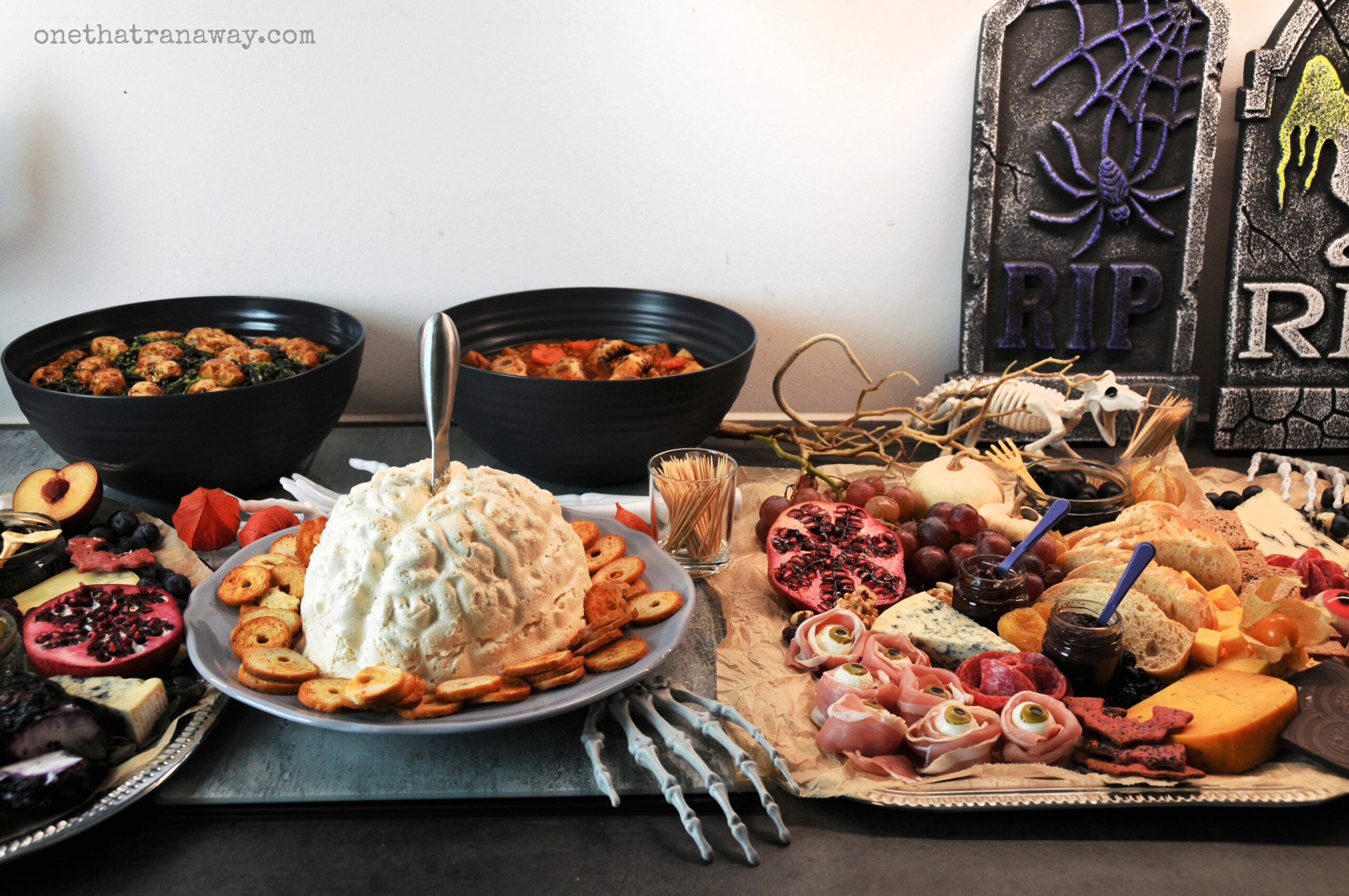 a Halloween themed cheese platter with a cream cheese brain, mozzarella eyeballs, bread and bat shaped crackers on a silver platter