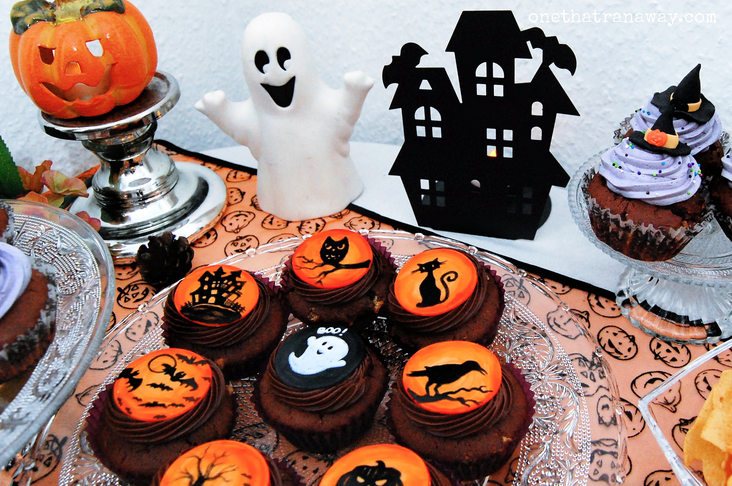 chocolate cupcakes with orange fondant toppers showing Halloween themed silhouettes on a table with Halloween decorations