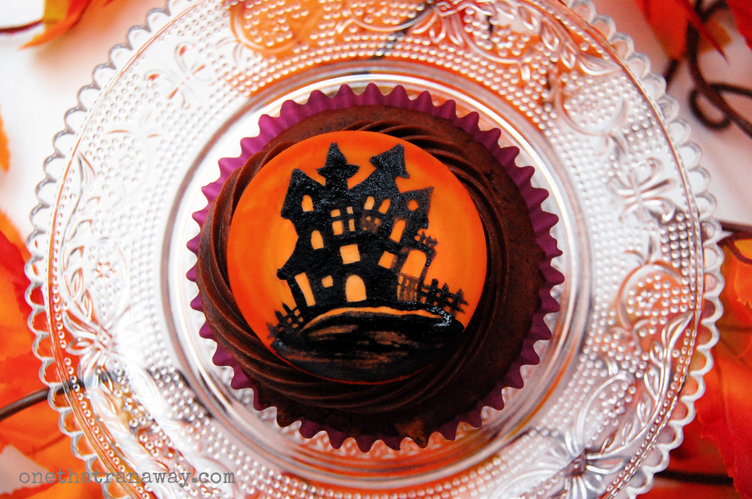chocolate cupcake with an orange fondant topper showing the silhouette of a haunted house
