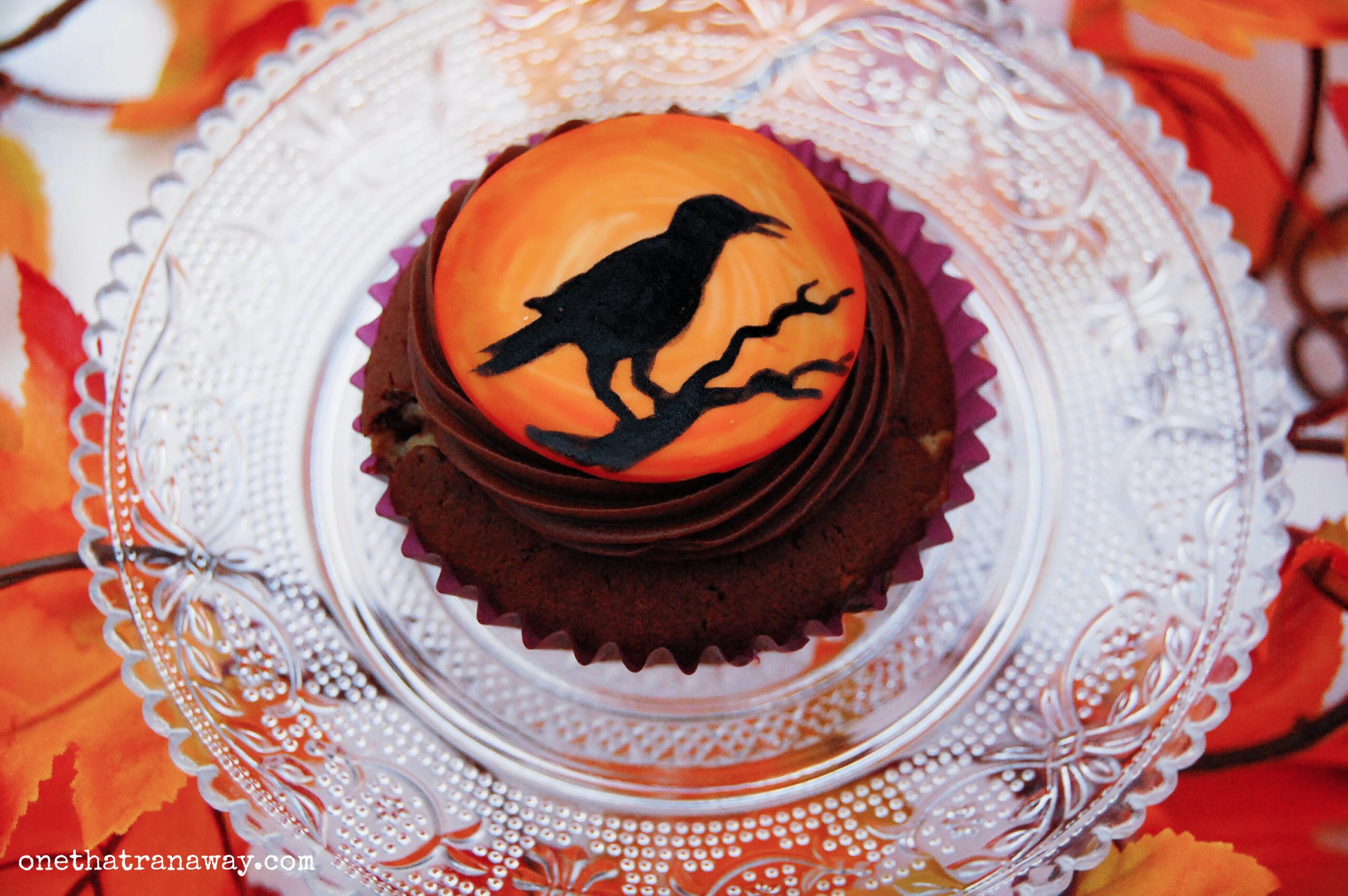chocolate cupcake with an orange fondant topper showing the silhouette of a raven