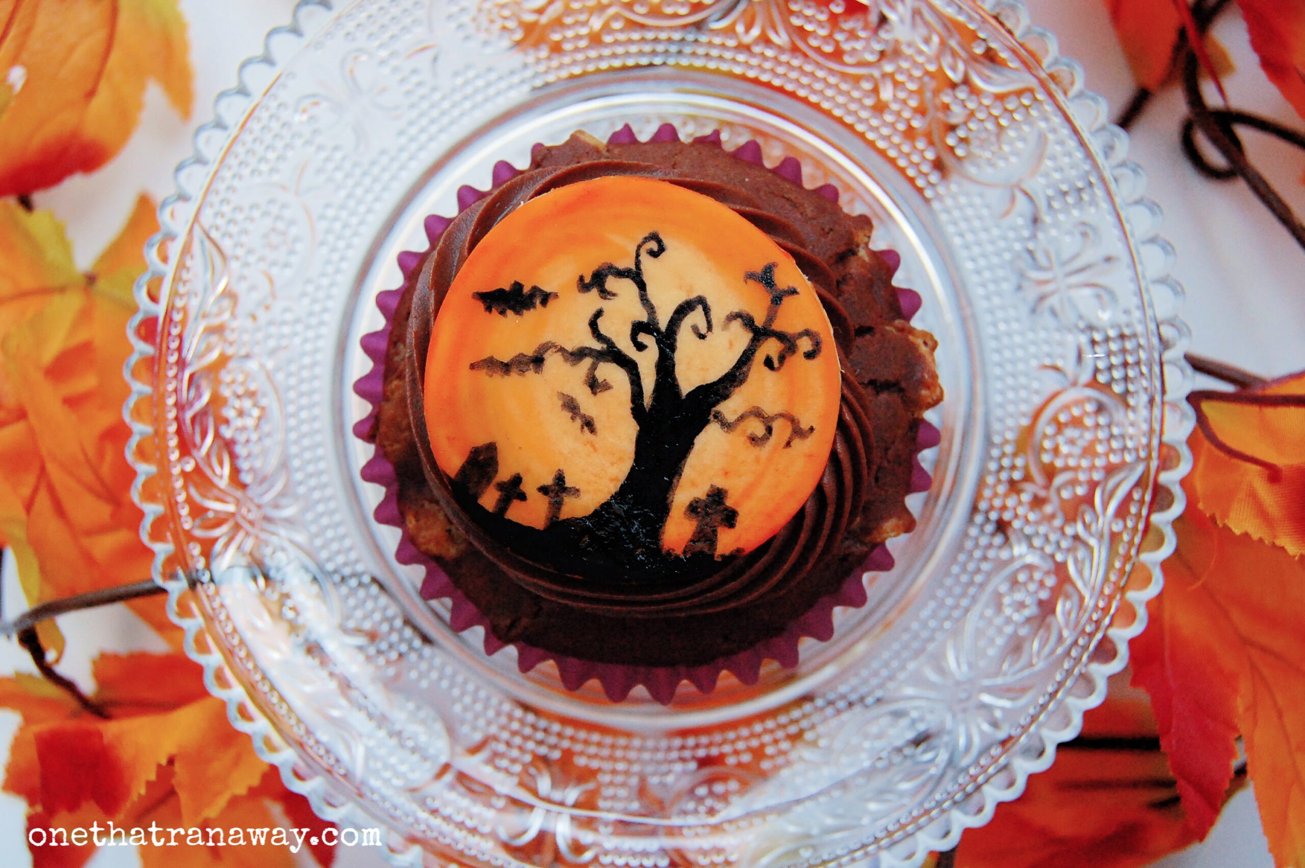 chocolate cupcake with an orange fondant topper showing the silhouette of a tree and graveyard