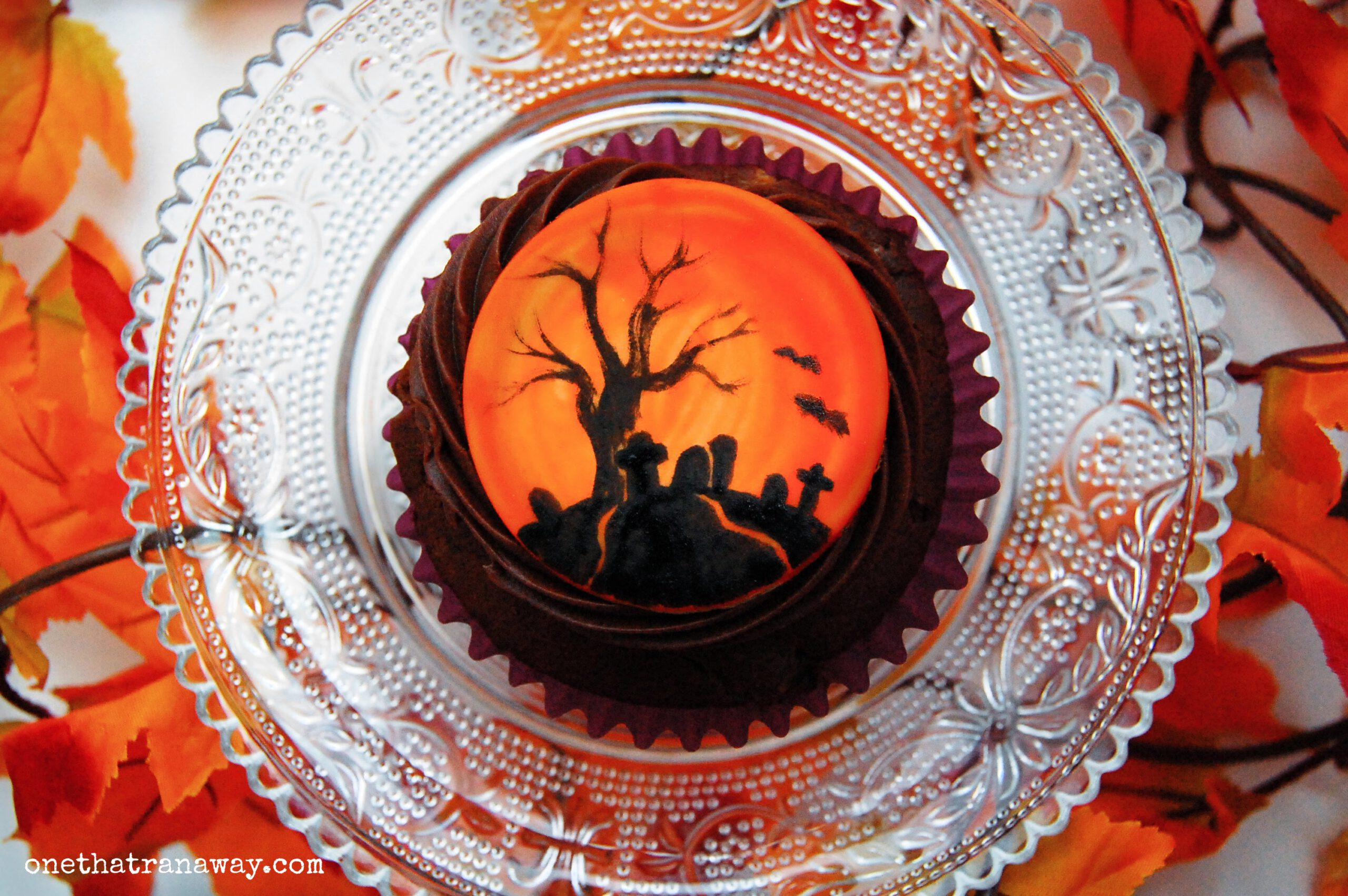 chocolate cupcake with an orange fondant topper showing the silhouette of a tree and graveyard